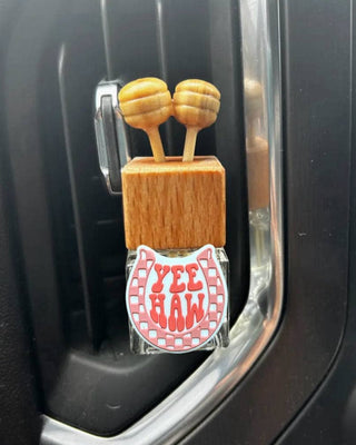 Car air freshener with wooden design and 'Yee Haw' label in a car's air vent.