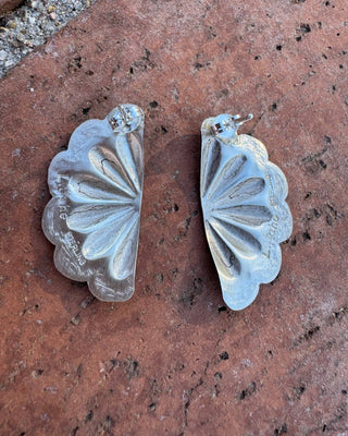Silver floral earrings on a textured brown surface