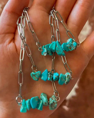 Turquoise stone and silver chain necklace held in a hand against a blurred background