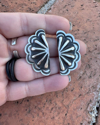 Pair of silver floral earrings held between fingers on a textured surface