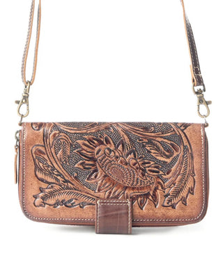 A brown tooled leather crossbody bag with an intricate floral and bird design, featuring a front strap closure and a gold-tone metal clasp, shown against a plain white background.