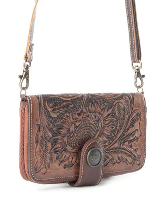 A brown tooled leather crossbody bag with floral engravings, a snap-button closure, and a matching leather strap on a white background.