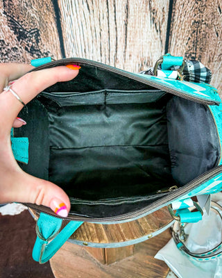 An open turquoise and white patterned handbag with a black interior lining, held open by a hand against a rustic wooden background.