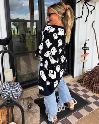 Woman wearing a black cardigan with white ghost patterns on a Halloween-themed porch.