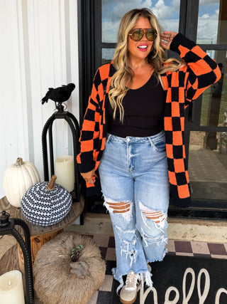Woman wearing an orange and black checkered cardigan in front of a door with Halloween decorations.