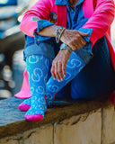 Model sitting on a ledge, posing in the High Maintenance Cowgirl Sky Blue Performance Socks.