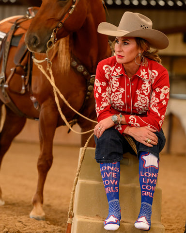 Model posing with horse while wearing the Long Live Cowgirls Red/Blue Performance Socks.