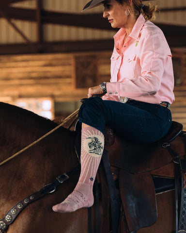 Model wearing the Bucking Dusty Pink Western Cowgirl Performance Socks while riding a horse.
