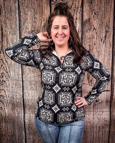 A model wearing the Down In The Hills Fitted Pullover with one hand on her hip and the other pulling back her hair in a wood back ground.