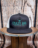 The Crazy Ass Cattle Trucker Cap displayed on a wooden table in a wood back ground.