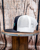 Side view of the Crazy Ass Cattle Trucker Cap displayed on a wooden table in a wood back ground.