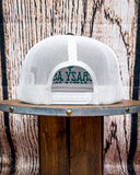 Back view of the Crazy Ass Cattle Trucker Cap showing the mesh back, displayed on a wooden table in a wood back drop.