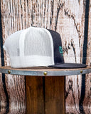 Side view of the Crazy Ass Cattle Trucker Cap displayed on a wooden table in a wood back ground.