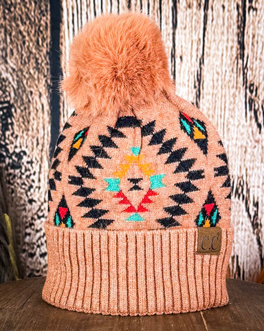 The Aztec Pom Beanie displayed on a wood table with a wood background.