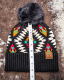 The Aztec Pom Beanie, shown on a cowhide backdrop with a ruler indicating it measures about 8 inches tall.