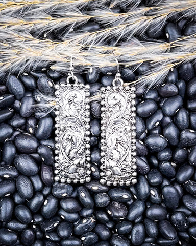 Silver earrings on black beans with wheat.