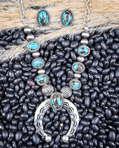 Necklace and earrings on black pebbles and wheat.