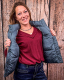 A girl modeling the Jolie Hooey Reversible Puffer Vest. She is holding the vest open to show the gray color inside. She is standing in front of a wood backdrop.