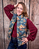 A girl modeling the Jolie Hooey Reversible Puffer Vest. The vest is open and she is wearing a red sweater underneath. She has one hand on her hip and one on her head. She is standing in front of a wood backdrop. 