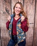  A girl modeling the Jolie Hooey Reversible Puffer Vest. The vest is open and she is wearing a red sweater underneath. She is holding the collar of the vest with both of her hands. She is standing in front of a wood backdrop.