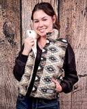 A girl modeling the Jane Hooey Reversible Puffer Vest with one hand in her pocket and the other is holding the collar of the vest. The vest is open, showing a sweater underneath. There is a wood backdrop behind her.