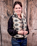 A girl modeling the Jane Hooey Reversible Puffer Vest with both hands gripping the inner sides of the vest. She is standing in front of a wood backdrop.