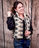 A girl modeling the Jane Hooey Reversible Puffer Vest with one hand holding the vest at the bottom and the other is twirling her hair. She is standing in front of a wood backdrop.