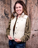 A girl modeling the Jane Hooey Reversible Puffer Vest. It is turned inside out to show the reversable design of the vest. She is holding the bottom of the vest and standing in front of a wood backdrop.