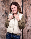 A girl modeling the Jane Hooey Reversible Puffer Vest, it is turned inside out to show the reversable design of the vest. it is buttoned up and she is holding the collar of the vest with both of her hands. She is standing in front of a wood backdrop.