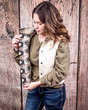 A girl wearing the Jane Hooey Reversible Puffer Vest, it is turned inside out to show the reversable design of the vest. She is holding the vest open to show the Aztec like design on the inside. She is standing in front of a wood backdrop.