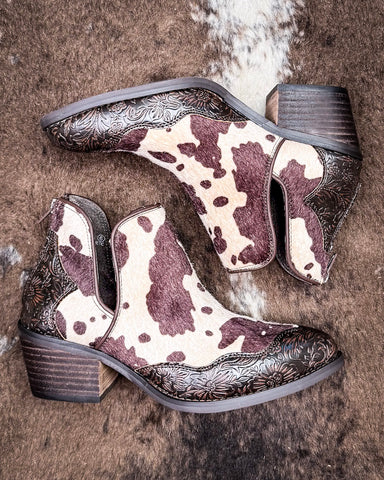 Pair of cow print patterned boots with decorative embossing on a textured surface