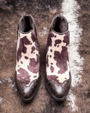 Pair of brown and white cow print boots on a textured surface