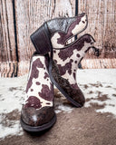 Pair of cow print boots with decorative patterns on a textured surface.