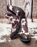 Pair of cow print boots with brown and white pattern on a wooden floor.