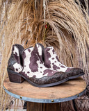 Pair of cow print patterned boots on a wooden stand with a rustic background