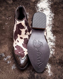 Cow print patterned boot with branded sole on a textured surface