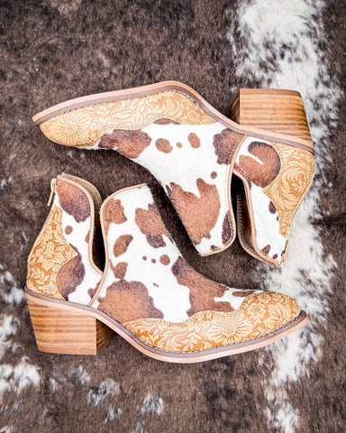 Pair of cow print ankle boots with decorative patterns on a textured surface