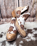 Cow print ankle boots with decorative brown sole on a textured surface