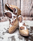 Cow print boots with tan embossed accents on a textured surface