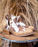 Cowboy booties with cow print and floral patterns on a wooden stand.