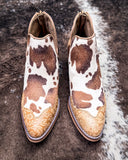 Pair of cow print boots with intricate designs on a textured surface