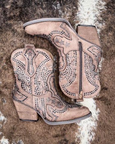 Pair of taupe cowboy boots with rhinestone details on a textured surface