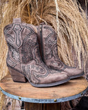Brown cowboy boots with intricate designs on a wooden platform against a rustic background