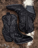 Black cowboy boots with rhinestone details on a textured surface