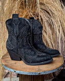 Black studded cowboy boots on a wooden stand with a rustic background