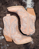 Beige cowboy boots with rhinestone detailing on a textured brown background