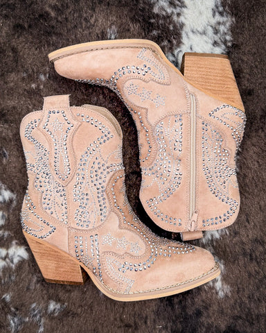 Beige cowboy boots with rhinestone detailing on a textured brown background