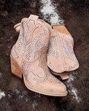 Beige cowboy boots with silver embellishments on a dark textured surface