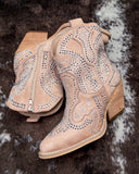 Beige cowboy boots with rhinestone detailing on a textured surface