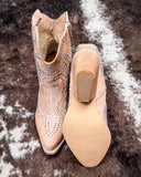 Pair of beige cowboy boots with rhinestone details on a textured surface